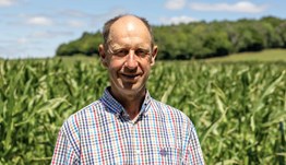 Headshot of a man (Jamie Butler) wearing a checked shirt stood in a field growing a tall crop.